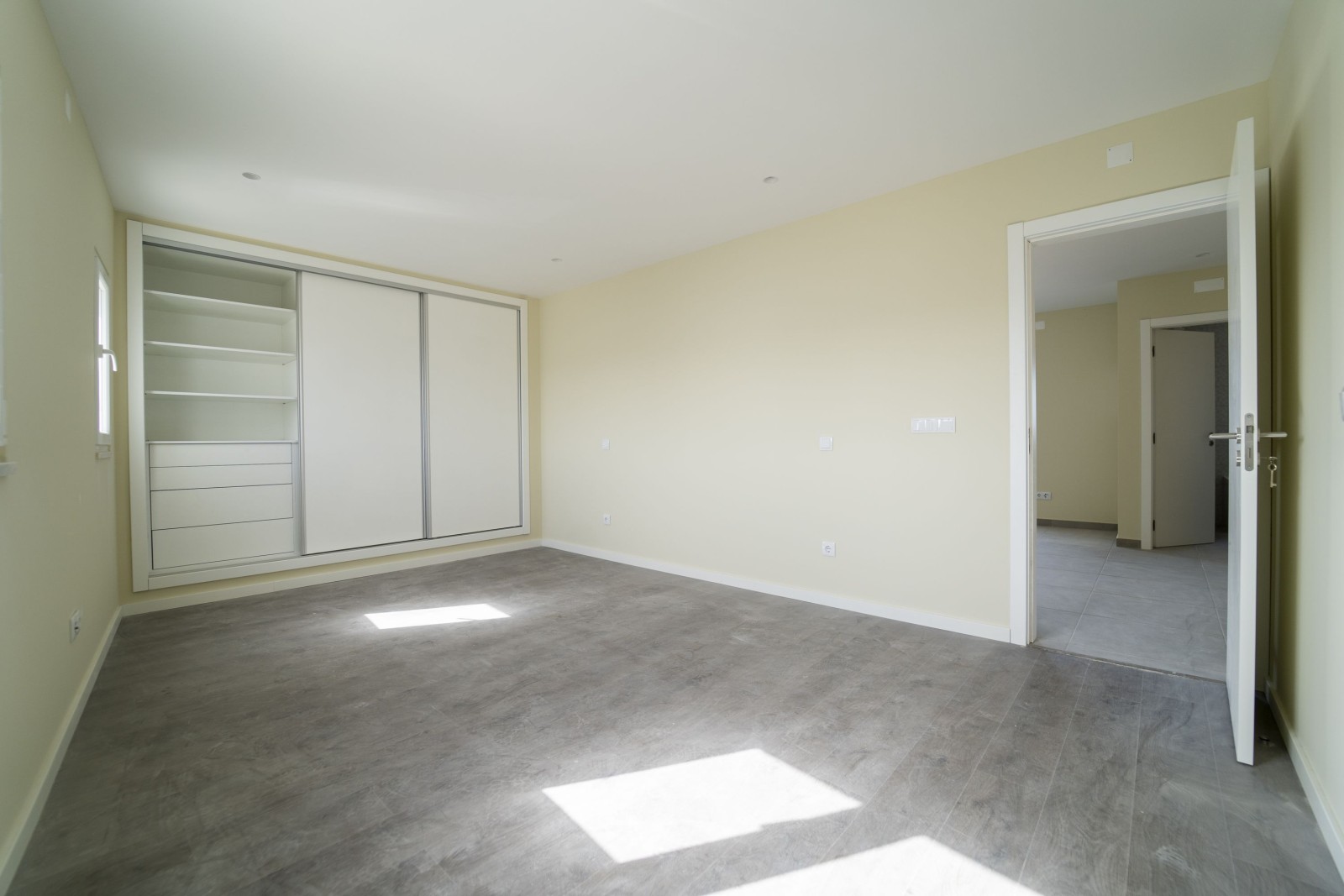 Pusty pokój z ciemną drewnianą podłogą laminowaną i szafą. Wnętrze domu, szeroka przestrzeń sypialni. Nowe, niedawno pomalowane mieszkanie lub dom. Drewniana podłoga. Zarządzanie nieruchomościami