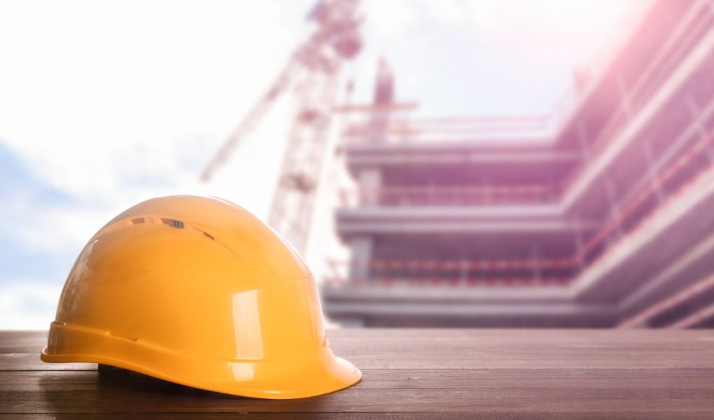 Kask na drewnianej powierzchni na placu budowy z niedokończonym budynkiem. Miejsce na tekst