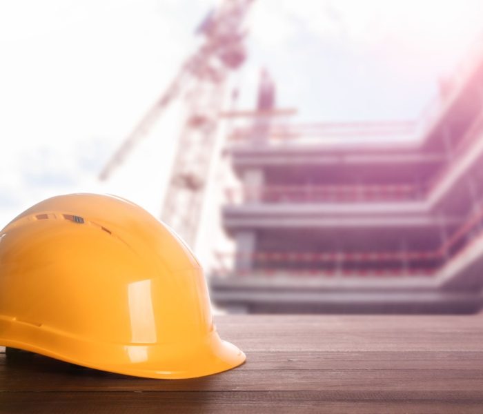 Kask na drewnianej powierzchni na placu budowy z niedokończonym budynkiem. Miejsce na tekst