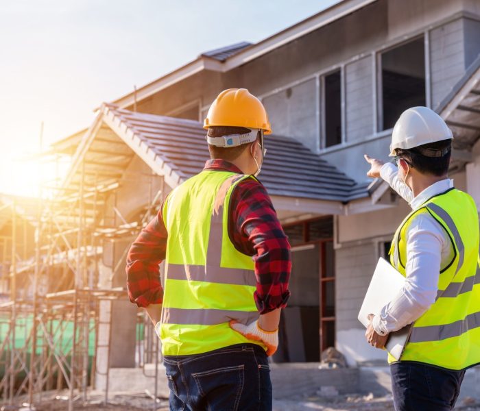 Architekt i inżynier budowlany oglądający niedokończony dom na placu budowy na zewnątrz. Koncepcja współpracy przy budowie budynku. Praca zespołowa