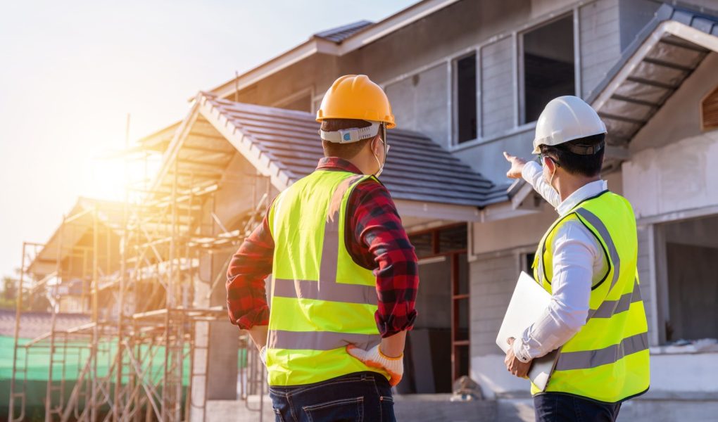 Architekt i inżynier budowlany oglądający niedokończony dom na placu budowy na zewnątrz. Koncepcja współpracy przy budowie budynku. Praca zespołowa