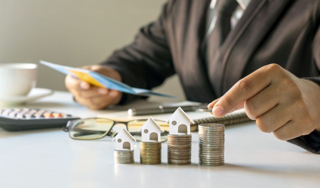 Biznesmen kładący monety na stosie monet z koncepcją finansową modelu domu. Hipoteka i hipoteka na nieruchomości