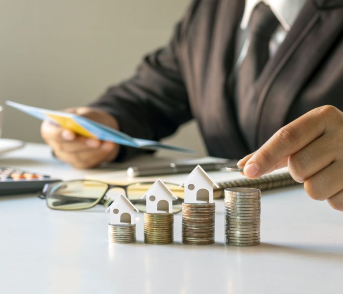Biznesmen kładący monety na stosie monet z koncepcją finansową modelu domu. Hipoteka i hipoteka na nieruchomości