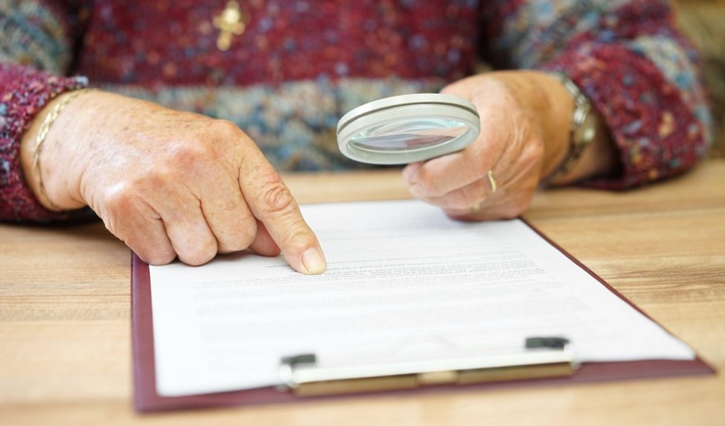 starsza osoba z lupą sprawdzająca dokument