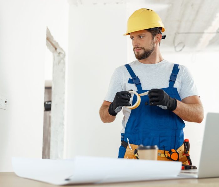 Zapracowany złota rączka, elektryk używający taśmy izolacyjnej podczas instalowania nowego gniazdka elektrycznego w mieszkaniu