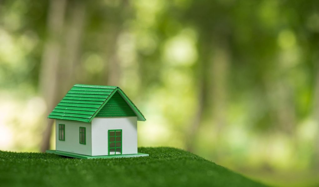 Przyjazny dla środowiska dom nieruchomości. Mały model domu nieruchomości na trawie w zielonej ekologii przyrody. Zrównoważony projekt mieszkaniowy oszczędzający energię i sprzedaż - wynajem koncepcji biznesowej