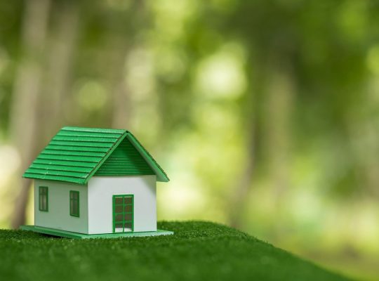 Przyjazny dla środowiska dom nieruchomości. Mały model domu nieruchomości na trawie w zielonej ekologii przyrody. Zrównoważony projekt mieszkaniowy oszczędzający energię i sprzedaż - wynajem koncepcji biznesowej