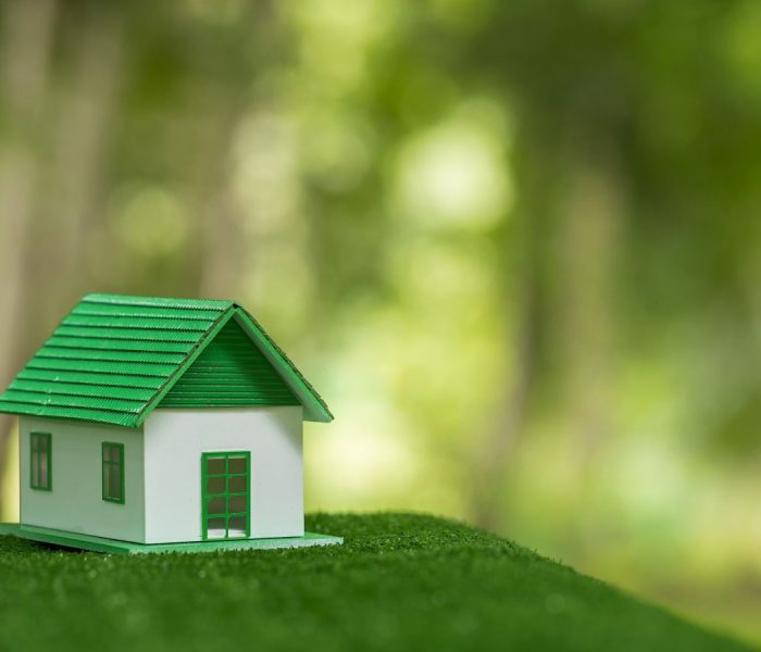 Przyjazny dla środowiska dom nieruchomości. Mały model domu nieruchomości na trawie w zielonej ekologii przyrody. Zrównoważony projekt mieszkaniowy oszczędzający energię i sprzedaż - wynajem koncepcji biznesowej