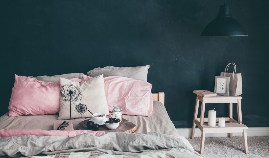 Czarno-różowa stylowa sypialnia na poddaszu. Niepościelone łóżko ze śniadaniem i lekturą na tacy. Lampa i wystrój wnętrza nad pustą ścianą tablicy z miejscem do kopiowania. Przytulna nowoczesna przestrzeń życiowa.