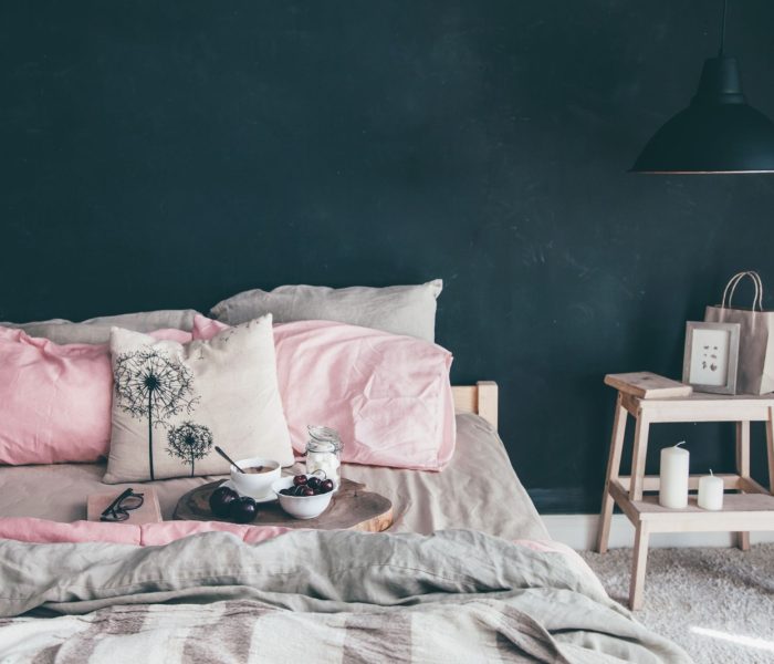 Czarno-różowa stylowa sypialnia na poddaszu. Niepościelone łóżko ze śniadaniem i lekturą na tacy. Lampa i wystrój wnętrza nad pustą ścianą tablicy z miejscem do kopiowania. Przytulna nowoczesna przestrzeń życiowa.