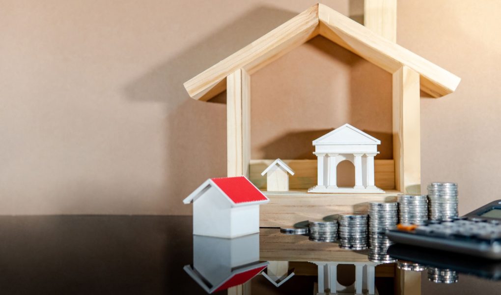 Koncepcja bankowości. Obliczanie oprocentowania kredytu. Oszczędzanie pieniędzy na inwestycje w nieruchomości lub rozwój nieruchomości. Hipoteka i wynajem domu. Moneta ułożone, dom i modele bankowe z kalkulatorem na stole.