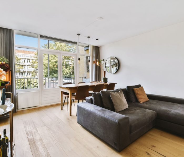 Wnętrze jasnego salonu ze stylowymi meblami i dekoracjami oraz szklanymi drzwiami i oknami prowadzącymi na balkon w słoneczny dzień