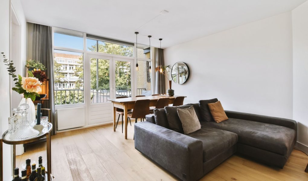 Wnętrze jasnego salonu ze stylowymi meblami i dekoracjami oraz szklanymi drzwiami i oknami prowadzącymi na balkon w słoneczny dzień