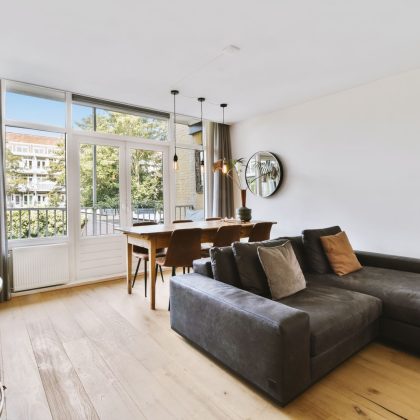 Wnętrze jasnego salonu ze stylowymi meblami i dekoracjami oraz szklanymi drzwiami i oknami prowadzącymi na balkon w słoneczny dzień