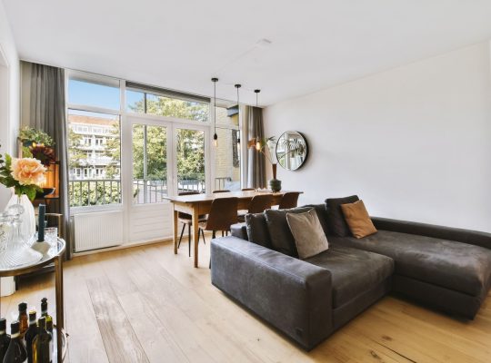 Wnętrze jasnego salonu ze stylowymi meblami i dekoracjami oraz szklanymi drzwiami i oknami prowadzącymi na balkon w słoneczny dzień