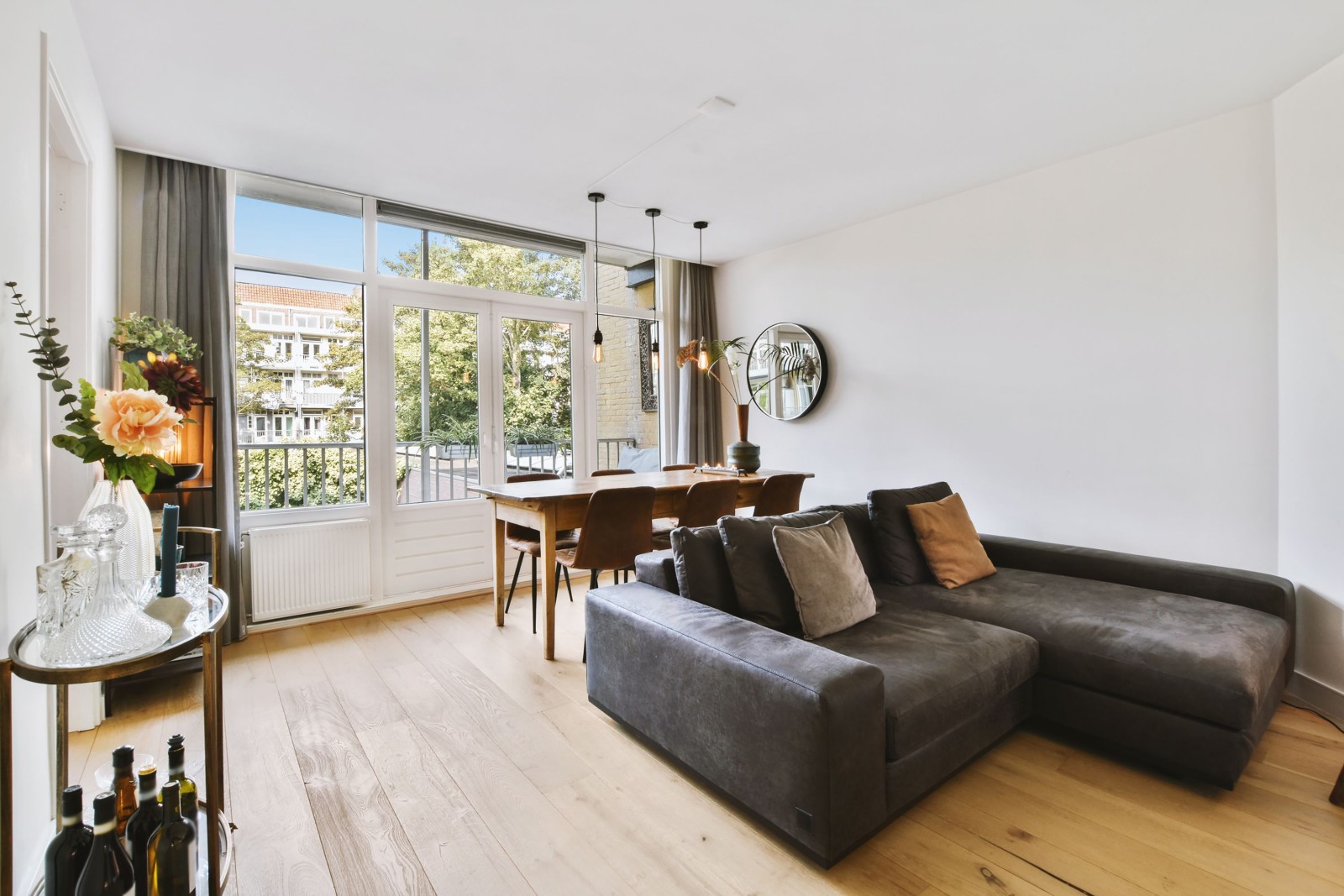 Wnętrze jasnego salonu ze stylowymi meblami i dekoracjami oraz szklanymi drzwiami i oknami prowadzącymi na balkon w słoneczny dzień