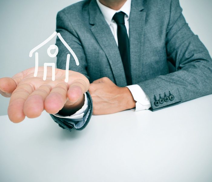 biznesmen siedzący przy biurku i trzymający w ręku rysunek domu