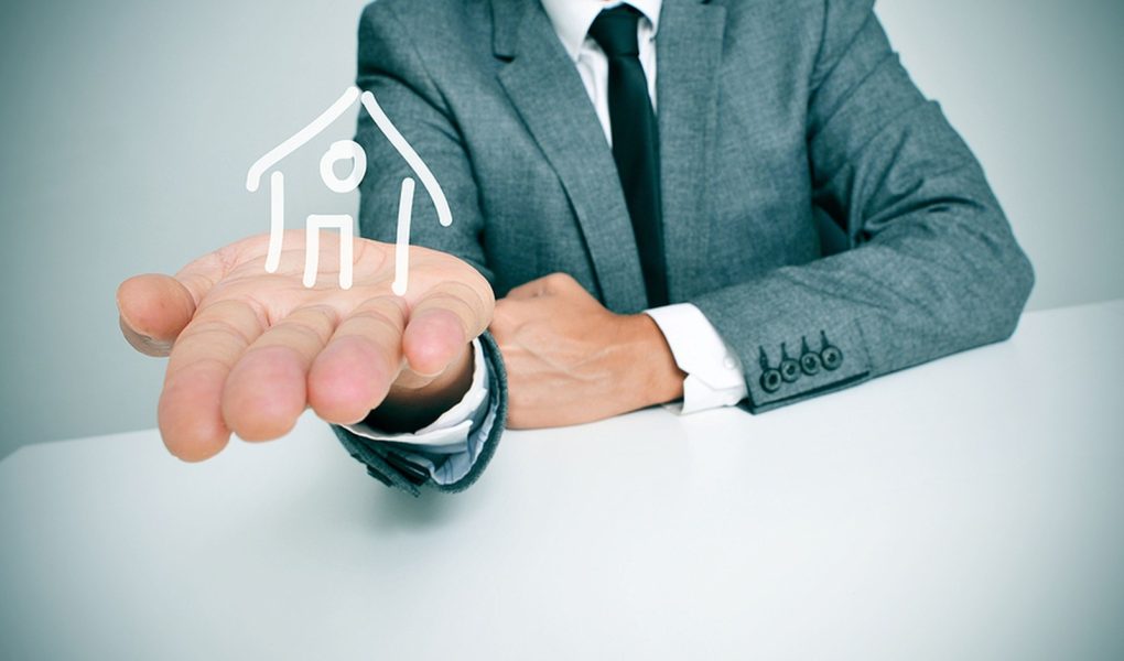 biznesmen siedzący przy biurku i trzymający w ręku rysunek domu