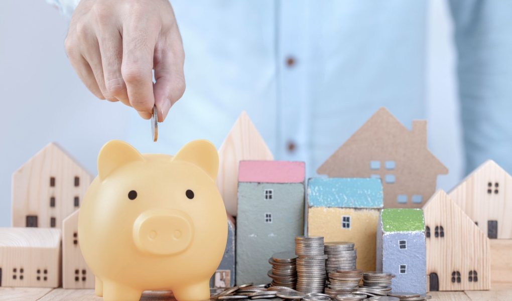 Biznesmen oszczędza pieniądze na skarbonce, planując przyszłość wynajmu mieszkania lub koncepcji domu. Ręcznie włóż monetę do skarbonki, aby zaoszczędzić na dom.