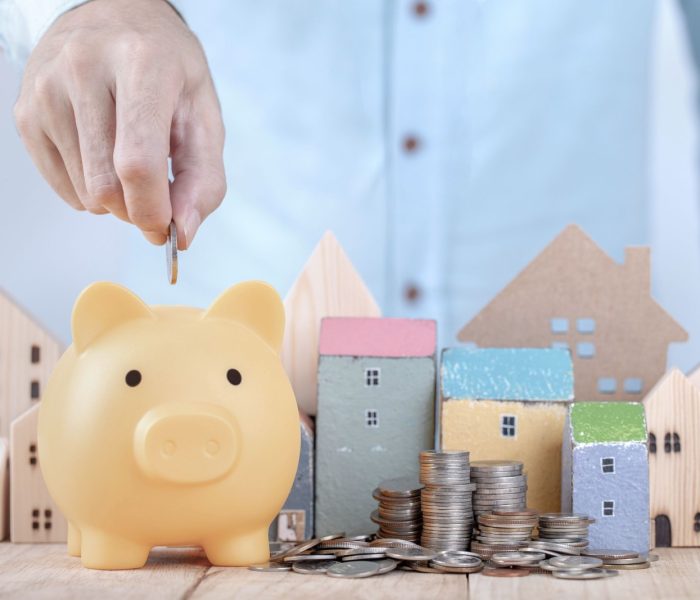 Biznesmen oszczędza pieniądze na skarbonce, planując przyszłość wynajmu mieszkania lub koncepcji domu. Ręcznie włóż monetę do skarbonki, aby zaoszczędzić na dom.