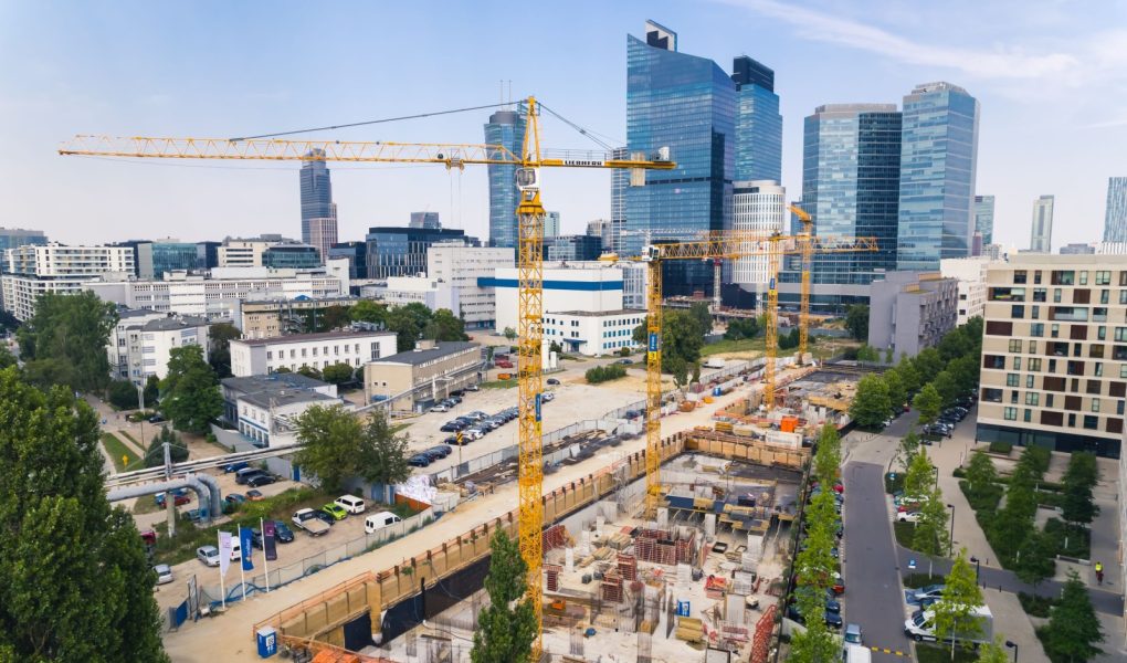 7.22.2022 Warszawa, Polska. Cztery żółte dźwigi budowlane na rozległym placu budowy pracujące nad nowym projektem. Wieżowce w tle. Koncepcja nowego osiedla. Zdjęcie wysokiej jakości