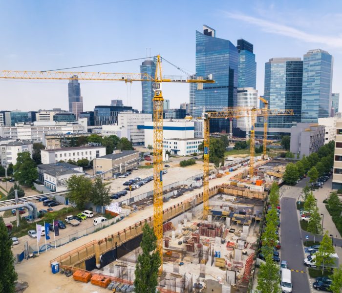 7.22.2022 Warszawa, Polska. Cztery żółte dźwigi budowlane na rozległym placu budowy pracujące nad nowym projektem. Wieżowce w tle. Koncepcja nowego osiedla. Zdjęcie wysokiej jakości