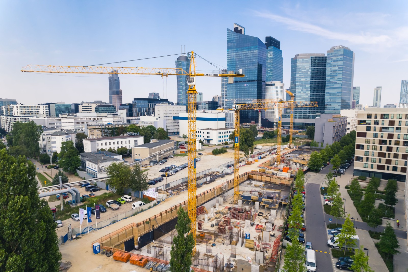 7.22.2022 Warszawa, Polska. Cztery żółte dźwigi budowlane na rozległym placu budowy pracujące nad nowym projektem. Wieżowce w tle. Koncepcja nowego osiedla. Zdjęcie wysokiej jakości