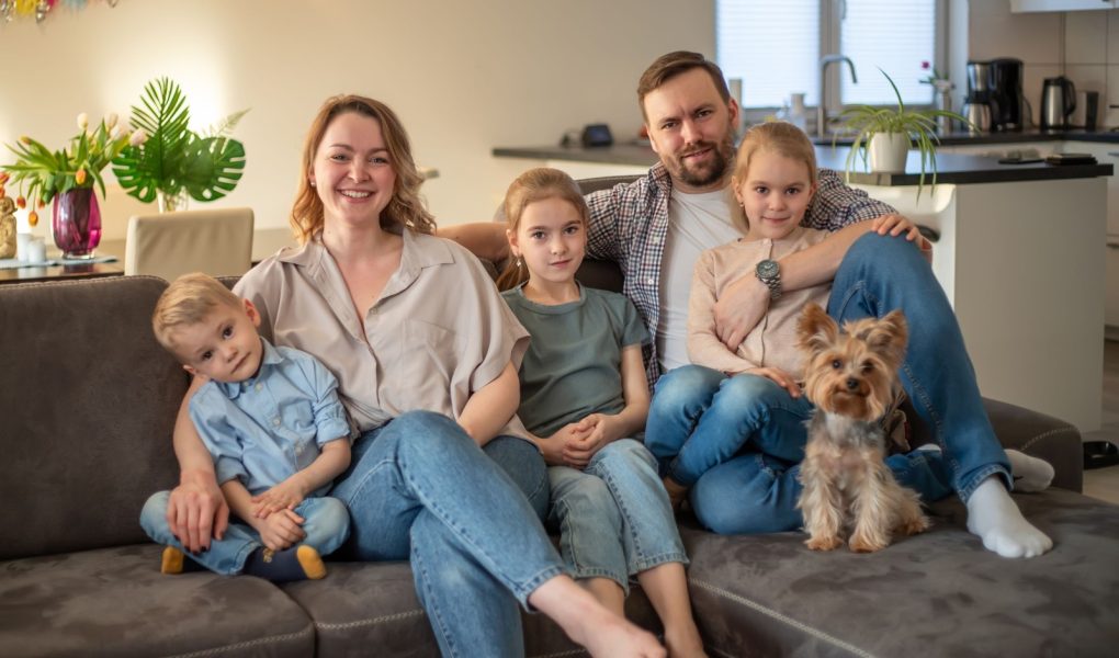 portret rodzinny. zdjęcie rodzinne, na którym mama, tata, córki, syn i pies uśmiechają się i przytulają na kanapie w przytulnej domowej atmosferze