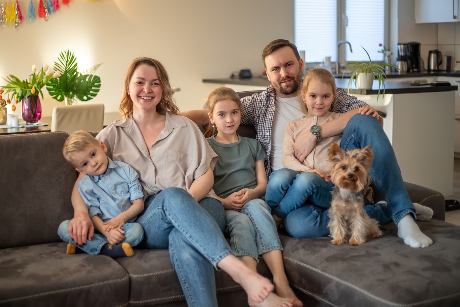 portret rodzinny. zdjęcie rodzinne, na którym mama, tata, córki, syn i pies uśmiechają się i przytulają na kanapie w przytulnej domowej atmosferze