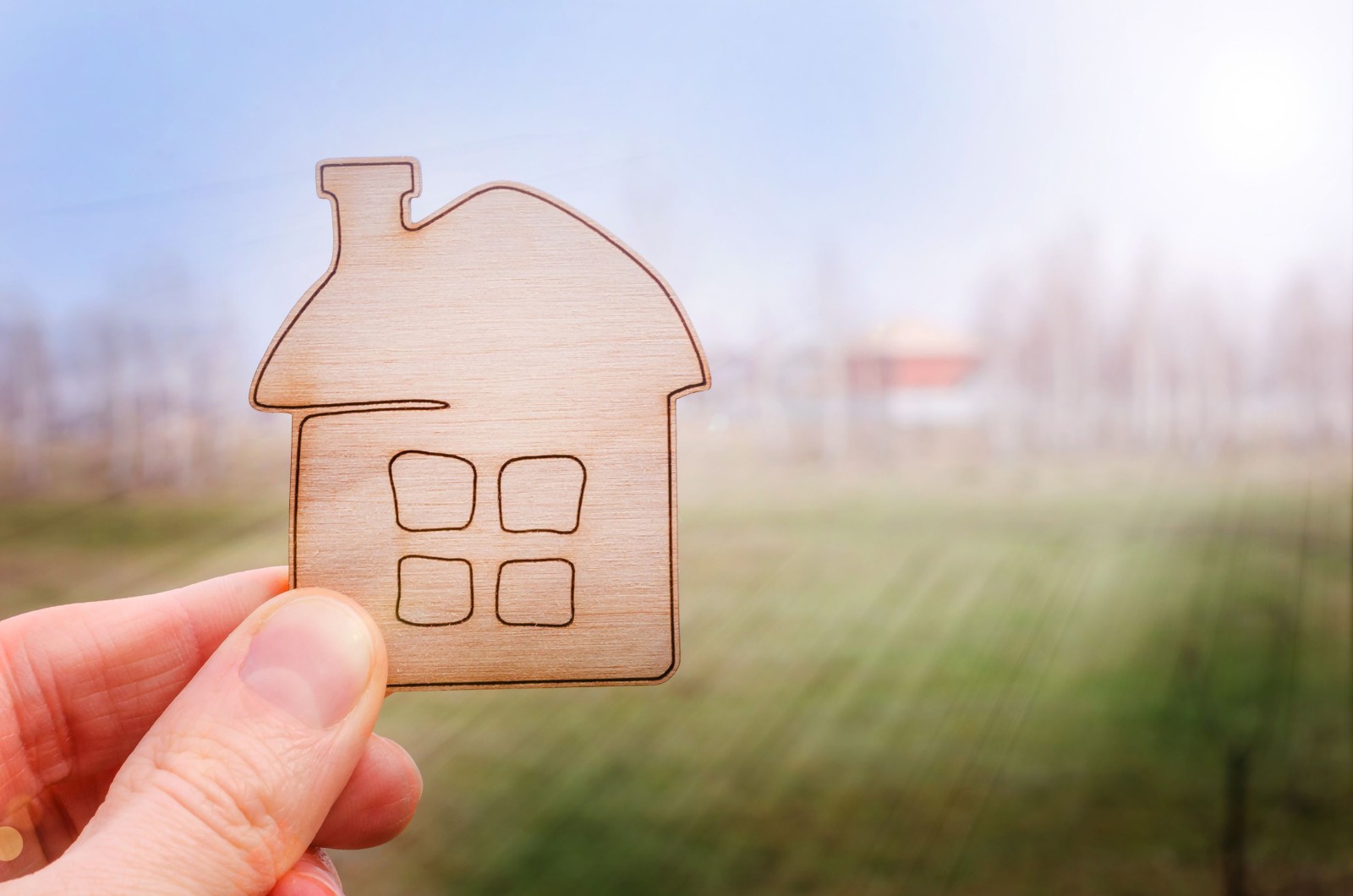 Model domu w ręku agenta nieruchomości lub osoby, która marzy o zakupie swojego domu na tle nieba i łąki z kopią przestrzeni. Oferta zakupu domu, ubezpieczenie nieruchomości, koncepcja przystępnych cenowo mieszkań.