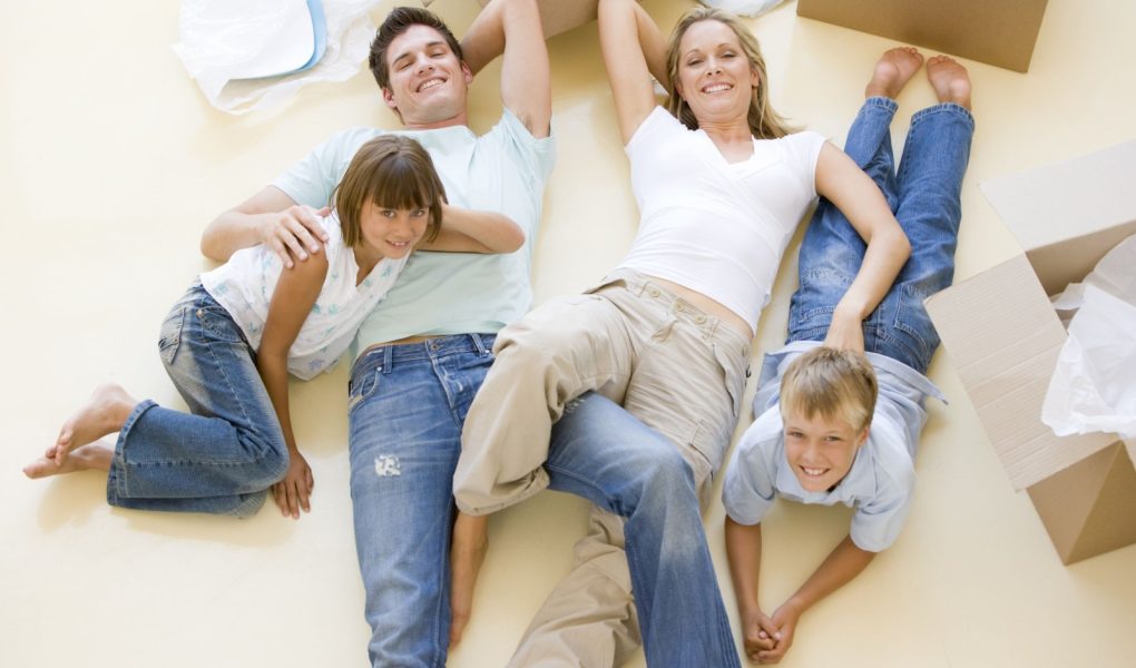 Uśmiechnięta rodzina leżąca na podłodze przy otwartych pudłach w nowym domu