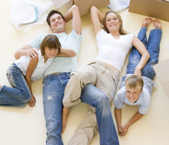 Uśmiechnięta rodzina leżąca na podłodze przy otwartych pudłach w nowym domu