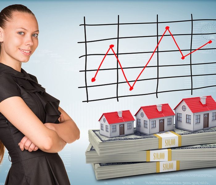 Bizneswoman uśmiecha się i stoi ze skrzyżowanymi ramionami. Pakiety dolarów z domami szeregowymi jako tło