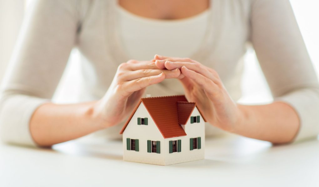 architektura, bezpieczeństwo, ochrona, nieruchomości i koncepcja nieruchomości - zbliżenie rąk chroniących model domu lub domu