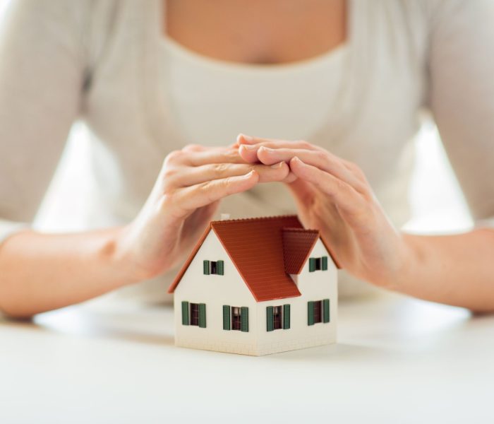 architektura, bezpieczeństwo, ochrona, nieruchomości i koncepcja nieruchomości - zbliżenie rąk chroniących model domu lub domu