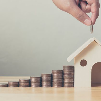 Inwestycja w nieruchomości i hipoteka na dom koncepcja finansowa Ręka wkładająca stos monet z drewnianym domem