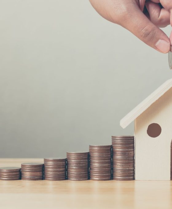 Inwestycja w nieruchomości i hipoteka na dom koncepcja finansowa Ręka wkładająca stos monet z drewnianym domem