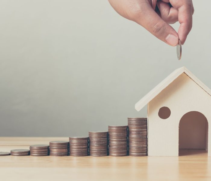 Inwestycja w nieruchomości i hipoteka na dom koncepcja finansowa Ręka wkładająca stos monet z drewnianym domem