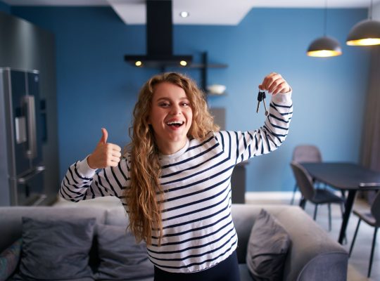 Szczęśliwa kobieta pokazująca klucze do nowego domu lub mieszkania w nowoczesnym wnętrzu. Kobieta najemca z nowymi kluczami do domu przenosi się do najmu. Pani kupiła nieruchomość, przeprowadza się. Koncepcja własności.