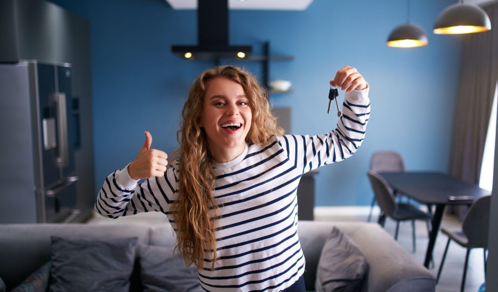 Szczęśliwa kobieta pokazująca klucze do nowego domu lub mieszkania w nowoczesnym wnętrzu. Kobieta najemca z nowymi kluczami do domu przenosi się do najmu. Pani kupiła nieruchomość, przeprowadza się. Koncepcja własności.