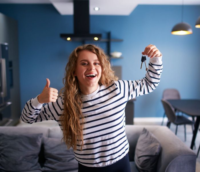 Szczęśliwa kobieta pokazująca klucze do nowego domu lub mieszkania w nowoczesnym wnętrzu. Kobieta najemca z nowymi kluczami do domu przenosi się do najmu. Pani kupiła nieruchomość, przeprowadza się. Koncepcja własności.