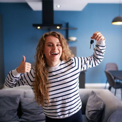 Szczęśliwa kobieta pokazująca klucze do nowego domu lub mieszkania w nowoczesnym wnętrzu. Kobieta najemca z nowymi kluczami do domu przenosi się do najmu. Pani kupiła nieruchomość, przeprowadza się. Koncepcja własności.
