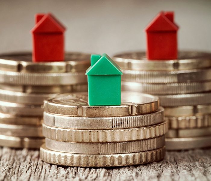 Miniaturowe domy spoczywające na stosach monet. Koncepcja hipotecznej drabiny nieruchomości i inwestycji w nieruchomości