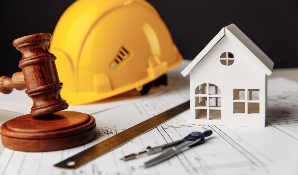 Sędziowski młotek, biały dom i żółty kask z narzędziami do rysowania na planie budowy. Koncepcja prawa