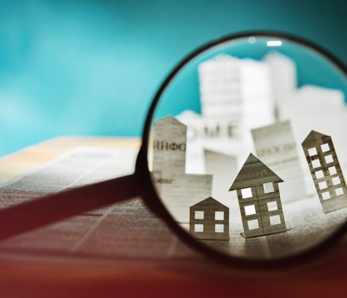 Szkło powiększające przed otwartą gazetą z papierowymi domami. Koncepcja wyszukiwania wynajem zakup nieruchomości.