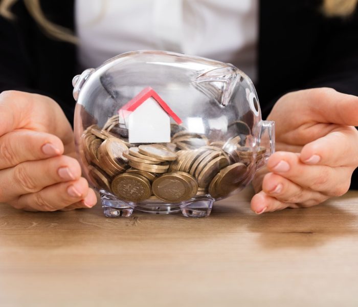Bizneswoman chroniąca swoje oszczędności z modelem domu w skarbonce. Koncepcja inwestycji w nieruchomości