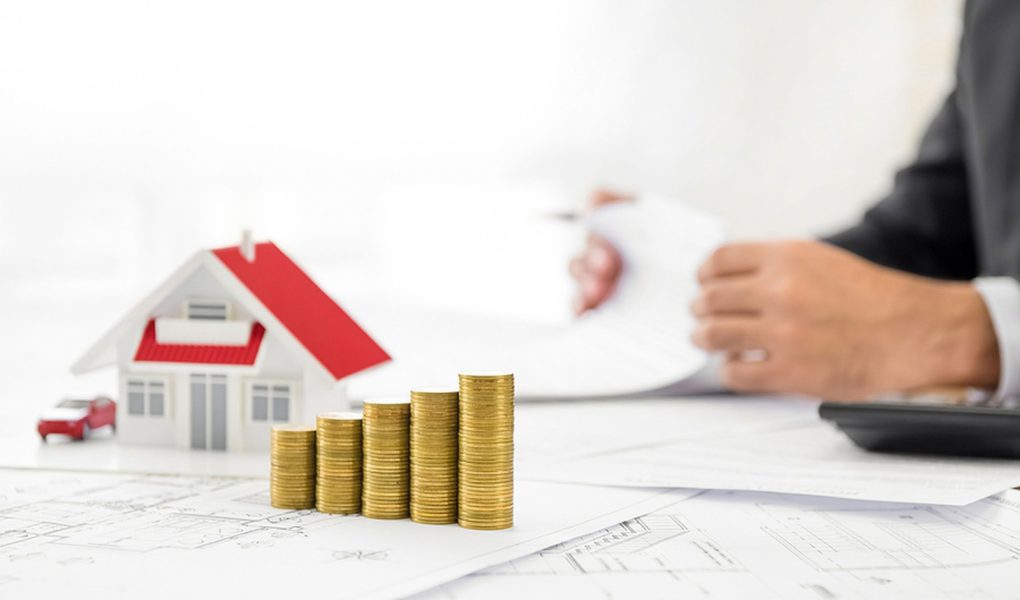 Pieniądze i model domu na papierze projektowym przy stole z rozmytym biznesmenem w tle - koncepcja finansowa nieruchomości i nieruchomości