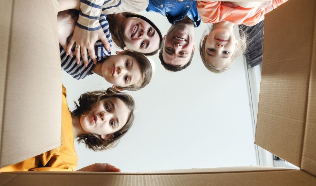 Szczęśliwa pięcioosobowa rodzina zaglądająca do kartonu. Młoda rodzina wyglądająca z kartonu i patrząca w kamerę. Radośni rodzice i dzieci bawiące się w pudełkach cieszą się przeprowadzką do nowego domu
