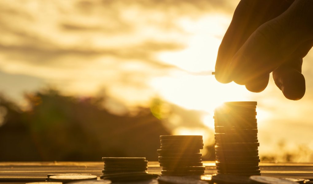 Koncepcja oszczędzania pieniędzy ustawiona przez męską rękę wkładającą stos monet do rosnącego biznesu. Close up of hand on sunset background, money concept, Business Finance and Money concept, Save money for prepare in the future. money silhouette.