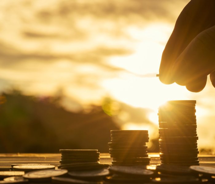 Koncepcja oszczędzania pieniędzy ustawiona przez męską rękę wkładającą stos monet do rosnącego biznesu. Close up of hand on sunset background, money concept, Business Finance and Money concept, Save money for prepare in the future. money silhouette.